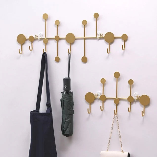 Wall-mounted black metal hook rack with decorative elements on a white wall.